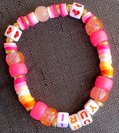 Bracelet in inspired by the colours of the lesbian flag, with the word yuri on it.